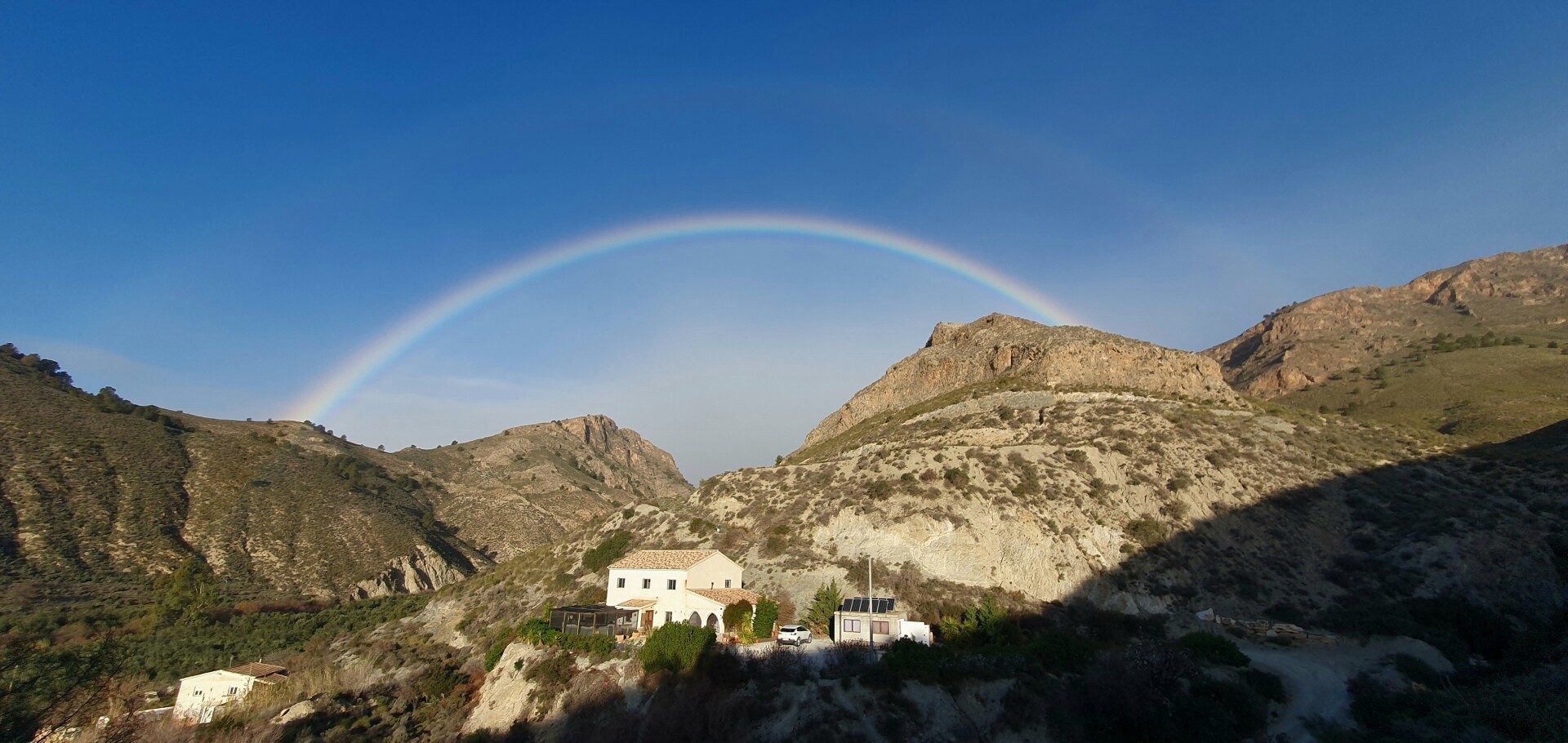 Arcoíris sobre unas montañas con una casa rural en primer plano.